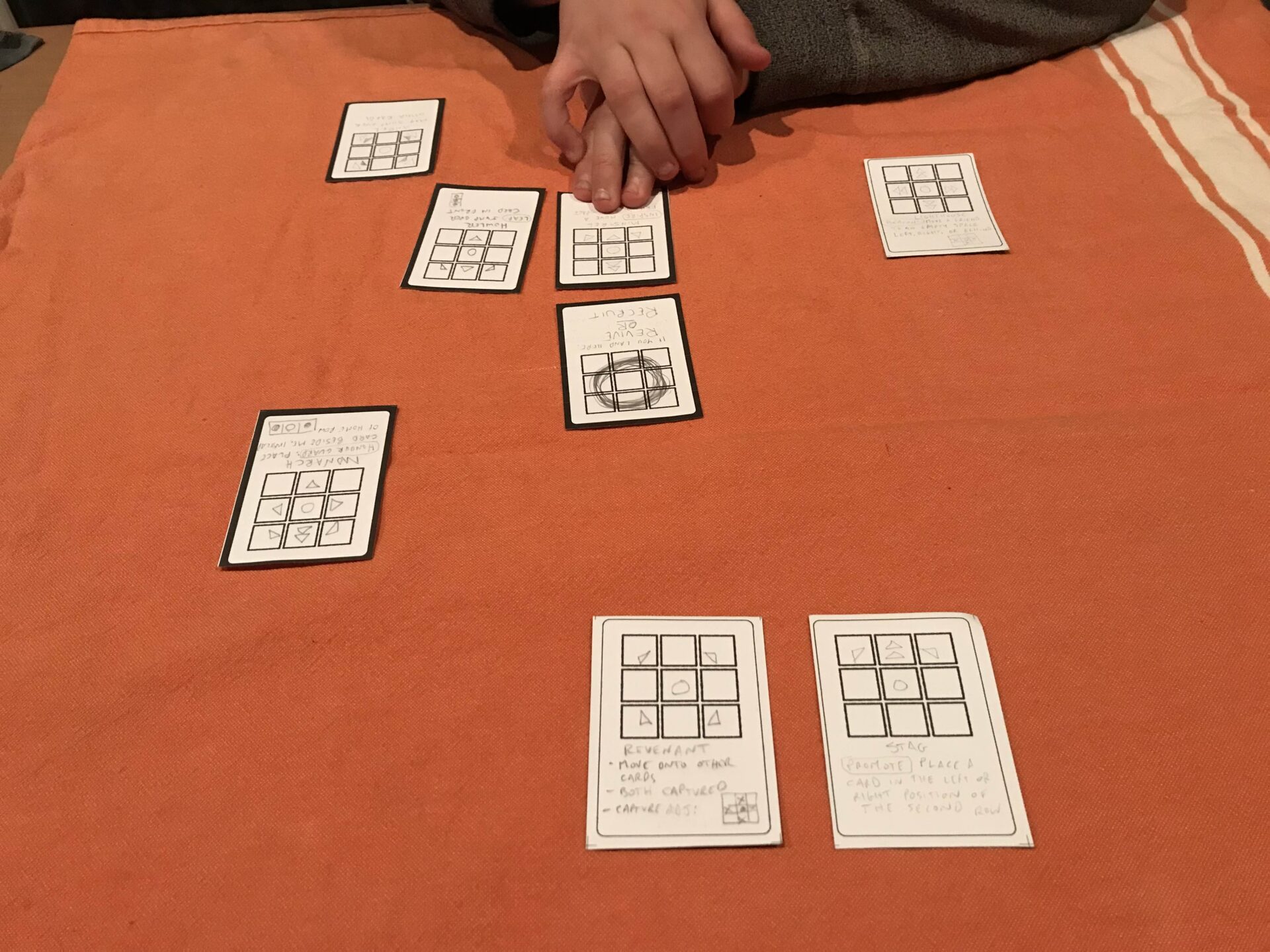 Playing that first protoype with my son. There are cards on the table; some have white borders and face me, the rest have black borders and face him. The centre card is in the middle. His hands are poised over a card on his side as he considers his next move.