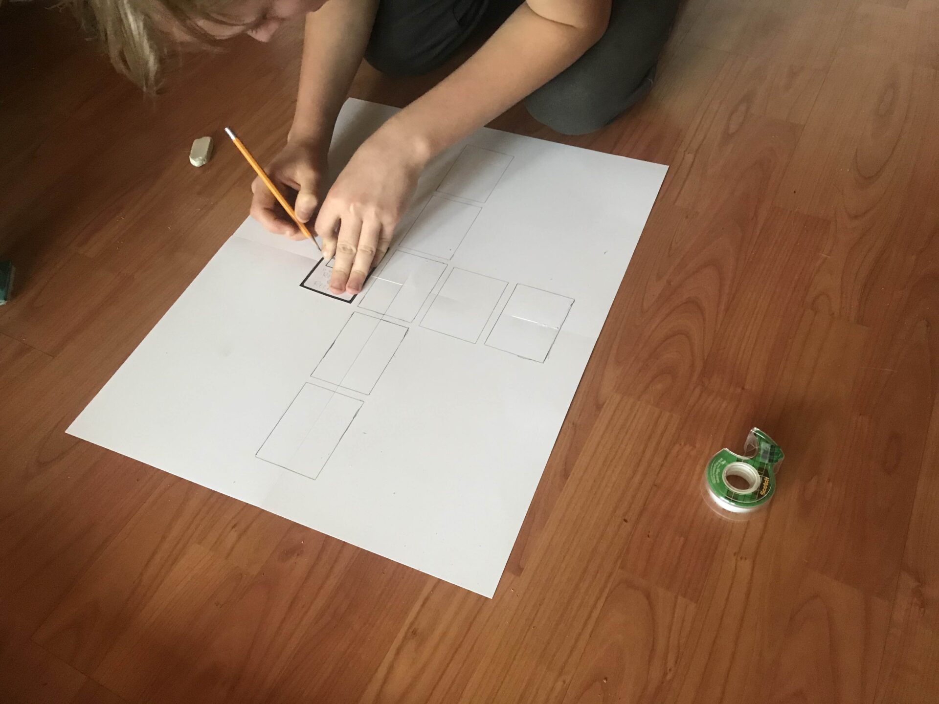 A teenage boy is tracing the outline of a card onto four pieces of cardstock that have been taped together.